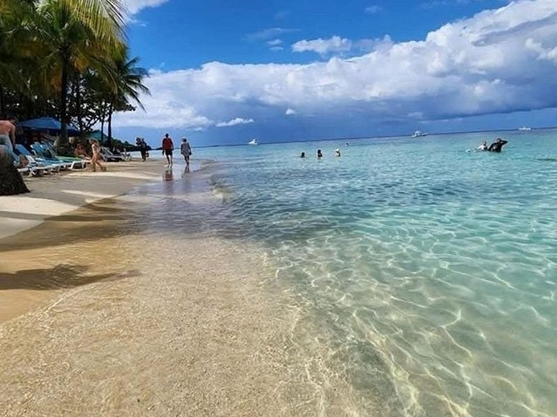 Clear, shallow water over rippled sand, bathers wading far along the beach