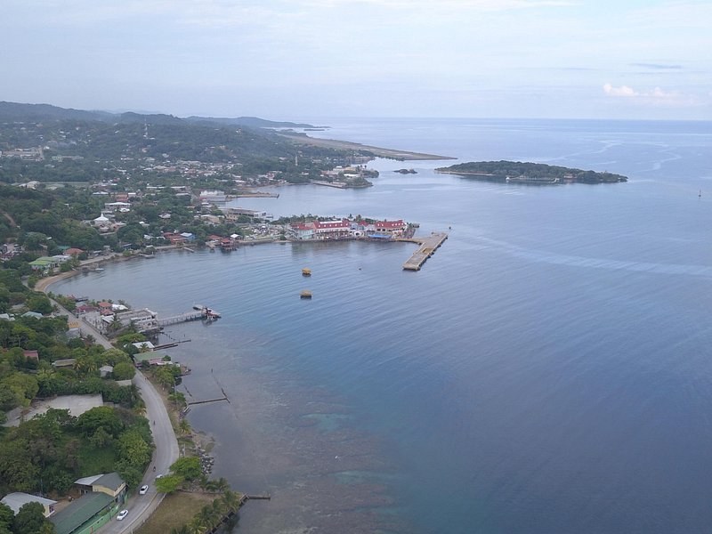 A harbour town curving round a bay, a long pier out into the water and a cay offshore