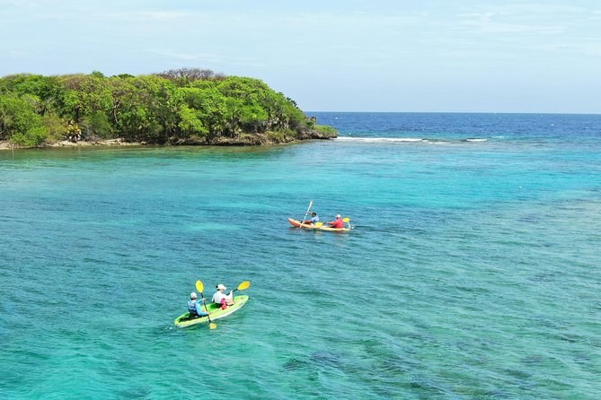 Two kayaks paddling across turquoise water towards a small green cay